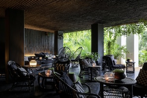 An outdoor seating area with wicker furniture, round tables, and potted plants. - Raya Heritage (Mae Rim)
