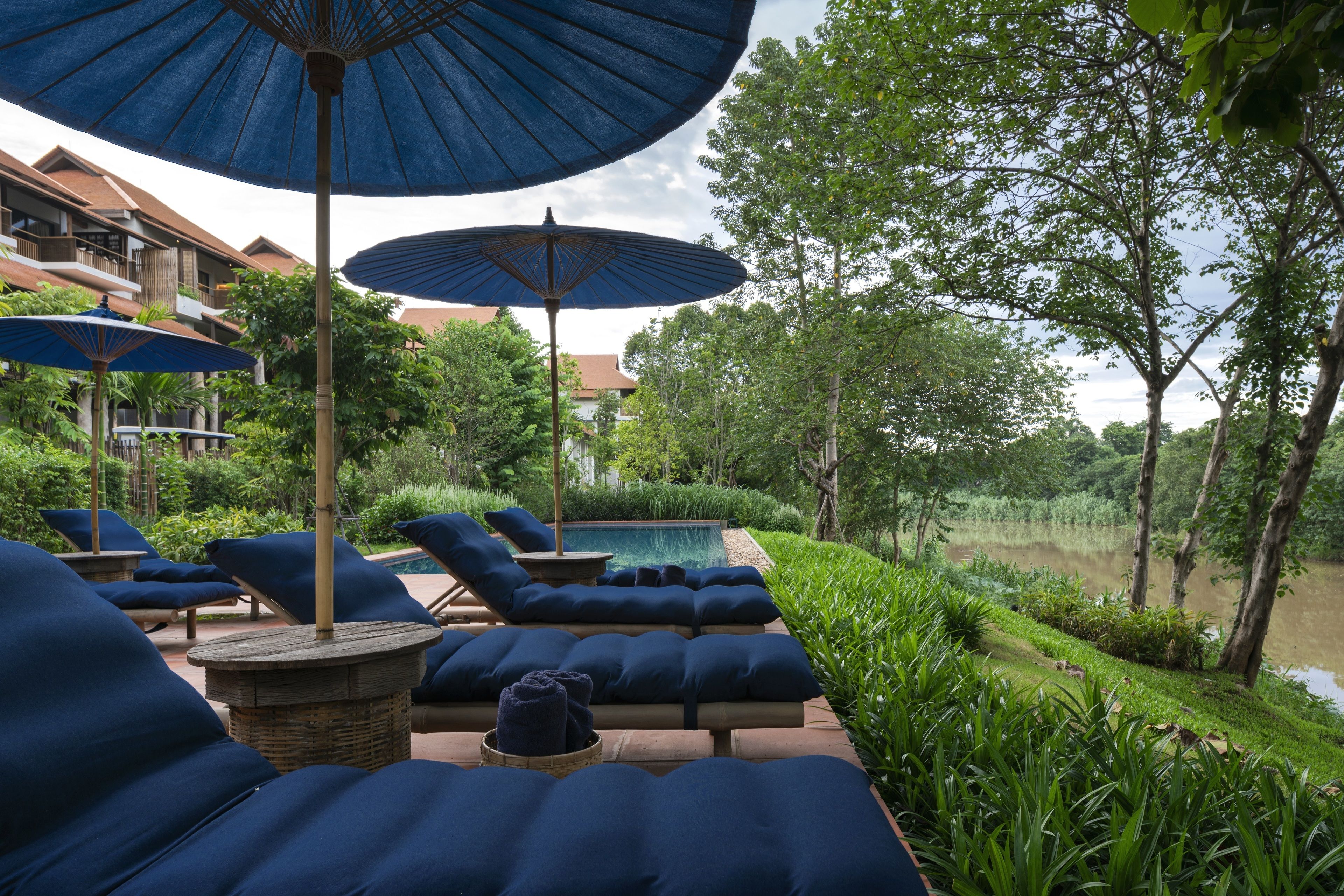 Un espace aménagé au bord de la piscine, avec des chaises longues et des parasols, entouré de verdure et bordé d’une étendue d’eau.