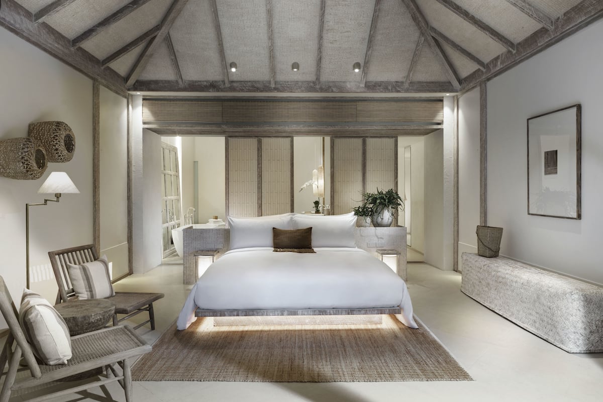 A spacious bedroom with a large bed, a sitting area with chairs, a bedside table, and a bench.