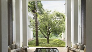 A modern interior with a central glass table, white columns, and a view of a green garden. - Raya Heritage (Mae Rim)