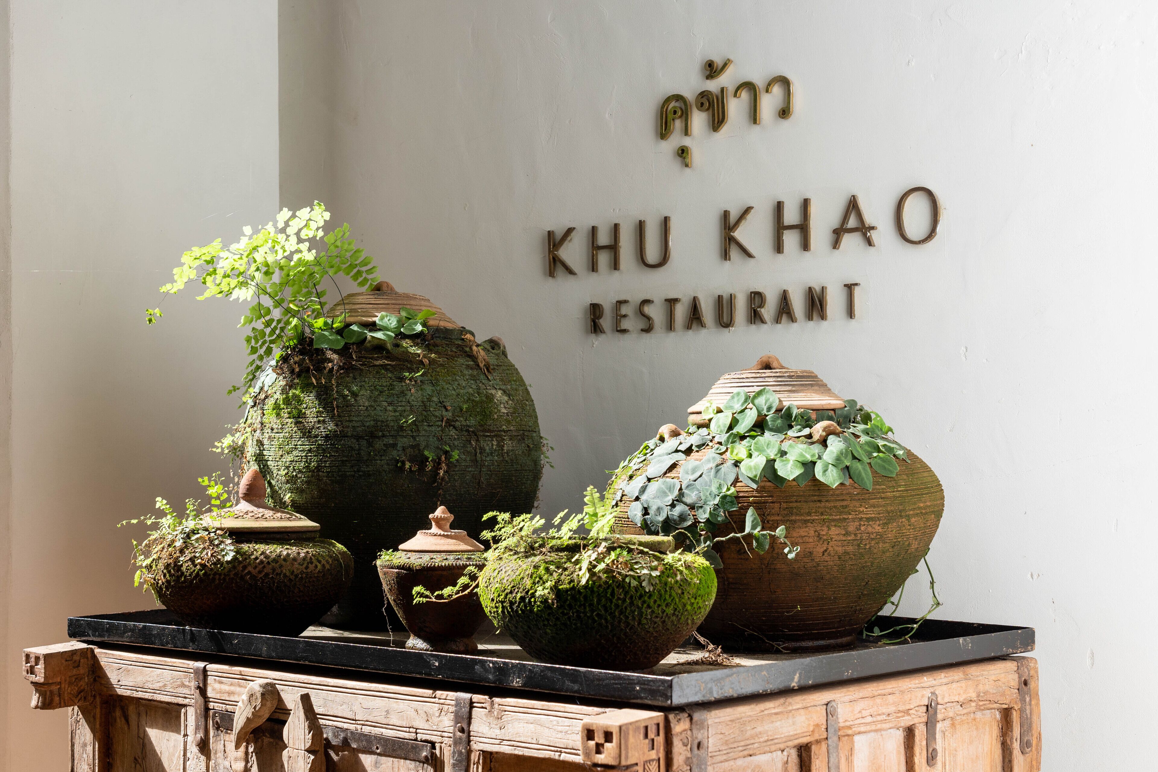 A wooden cabinet with potted plants and a sign for Khu Khao Restaurant.