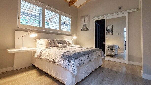 A bedroom with a bed, bedside lamps, a window with blinds, a door leading to another room, and a wall-mounted picture of the Eiffel Tower. - Umhlanga Lodge -No children (Umhlanga)