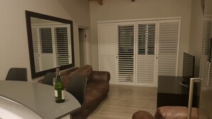 A living room with a brown leather sofa, a dining table with a bottle of wine, and a large mirror on the wall. - Umhlanga Lodge -No children (Umhlanga)