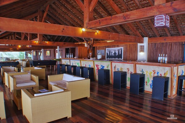 A spacious lounge area with wicker furniture, a bar with a mural, and wooden beams on the ceiling.