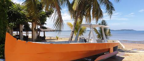 A boat parked on a sandy beach with palm trees and a clear view of the sea.