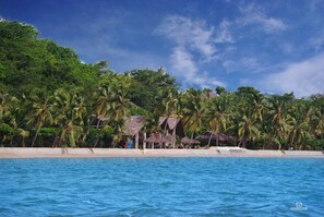 A beachfront property with thatched-roof structures, palm trees, and a sandy beach. - Anjiamarango Beach Resort (Nosy Be)