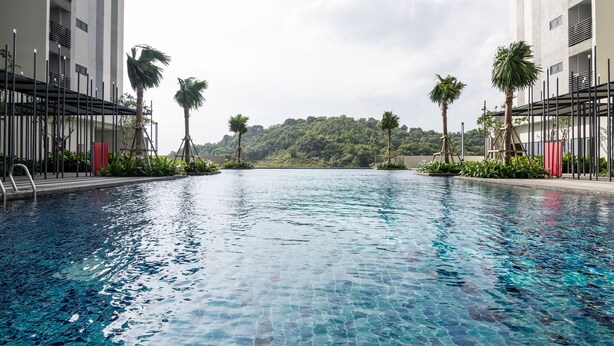 A swimming pool with clear water, surrounded by palm trees and a view of a forested hill. - Ramada by Wyndham Meridin Johor Bahru (Iskandar Puteri)
