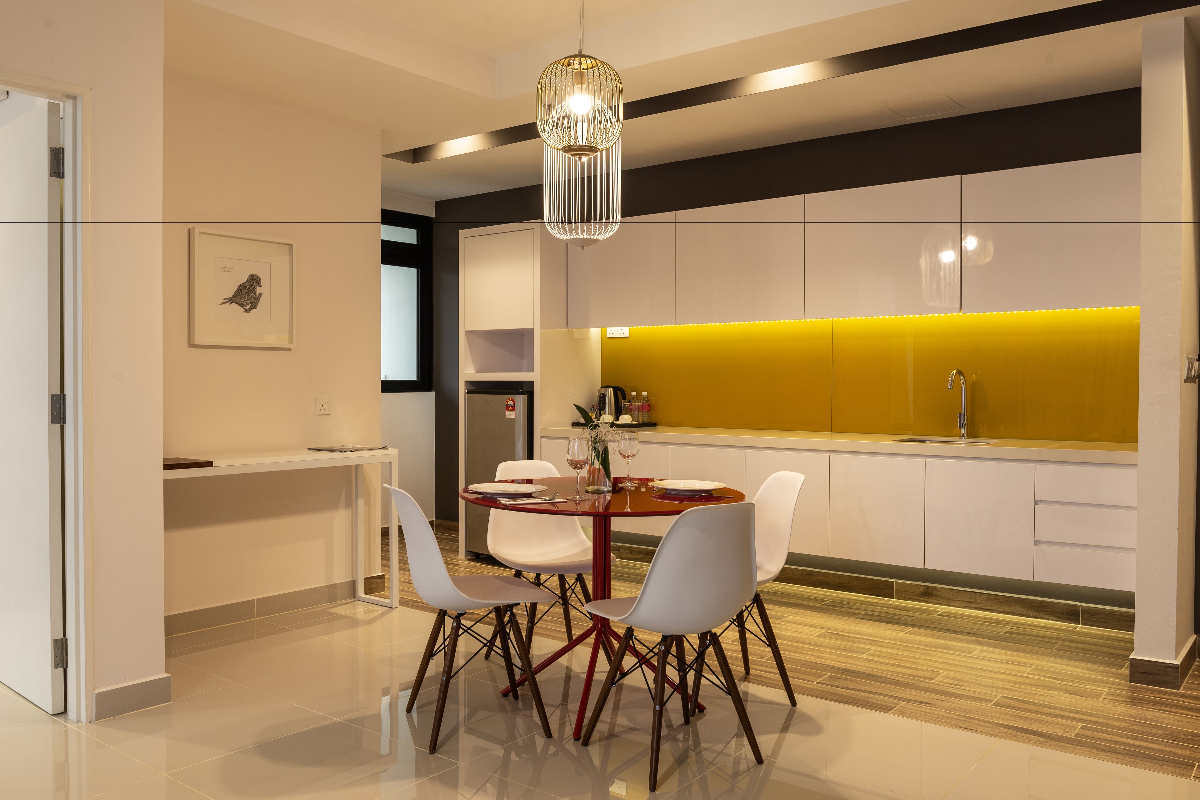 A modern kitchen with white cabinets, a yellow accent wall, and a dining area with a round table and white chairs.