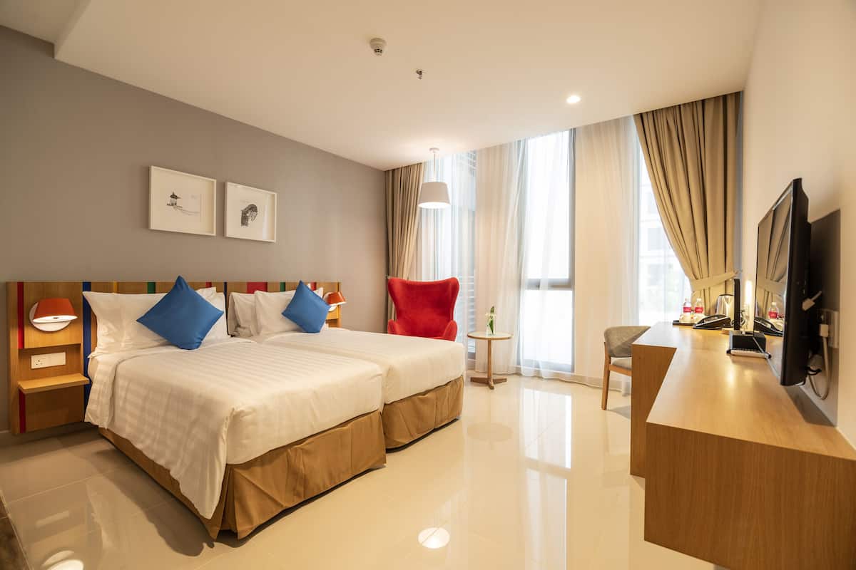 Ein Hotelzimmer mit zwei Betten, einem Schreibtisch, einem Fernseher und Bildern an der Wand.