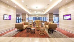 A spacious lobby with modern furnishings, including sofas and chairs, and a large window providing a view of the outside. - Ramada by Wyndham Meridin Johor Bahru (Iskandar Puteri)