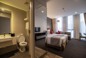 A modern hotel room with a bathroom, a bed, a TV, and a seating area.