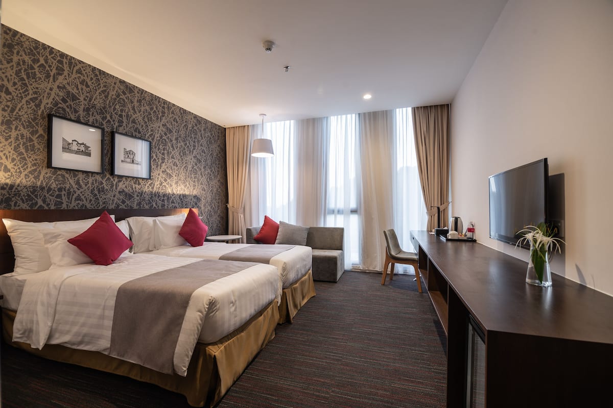 Ein Hotelzimmer mit zwei Betten, einem Schreibtisch, einem Fernseher und einem großen Fenster mit Vorhängen.