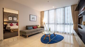 A modern hotel room with a bed, a sofa, a glass coffee table, and a large window with curtains.