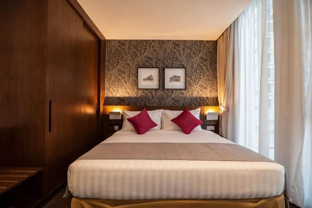 Ein Hotelzimmer mit einem großen Bett, zwei Nachttischen mit Lampen, einer Wand mit Muster und zwei gerahmten Bildern über dem Bett.