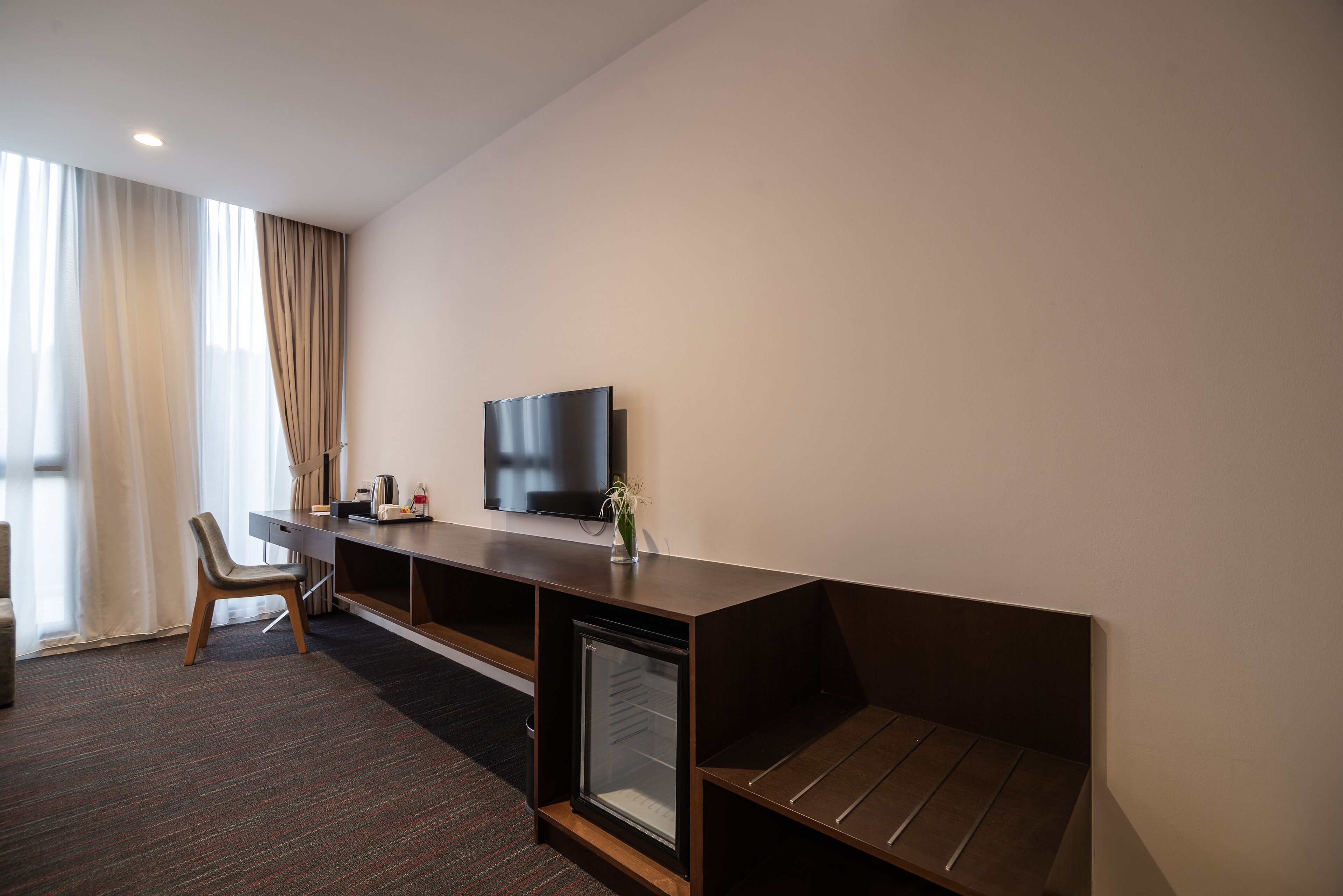 Une chambre d’hôtel moderne équipée d’un grand bureau, d’un téléviseur à écran plat, d’un petit réfrigérateur et d’une chaise.