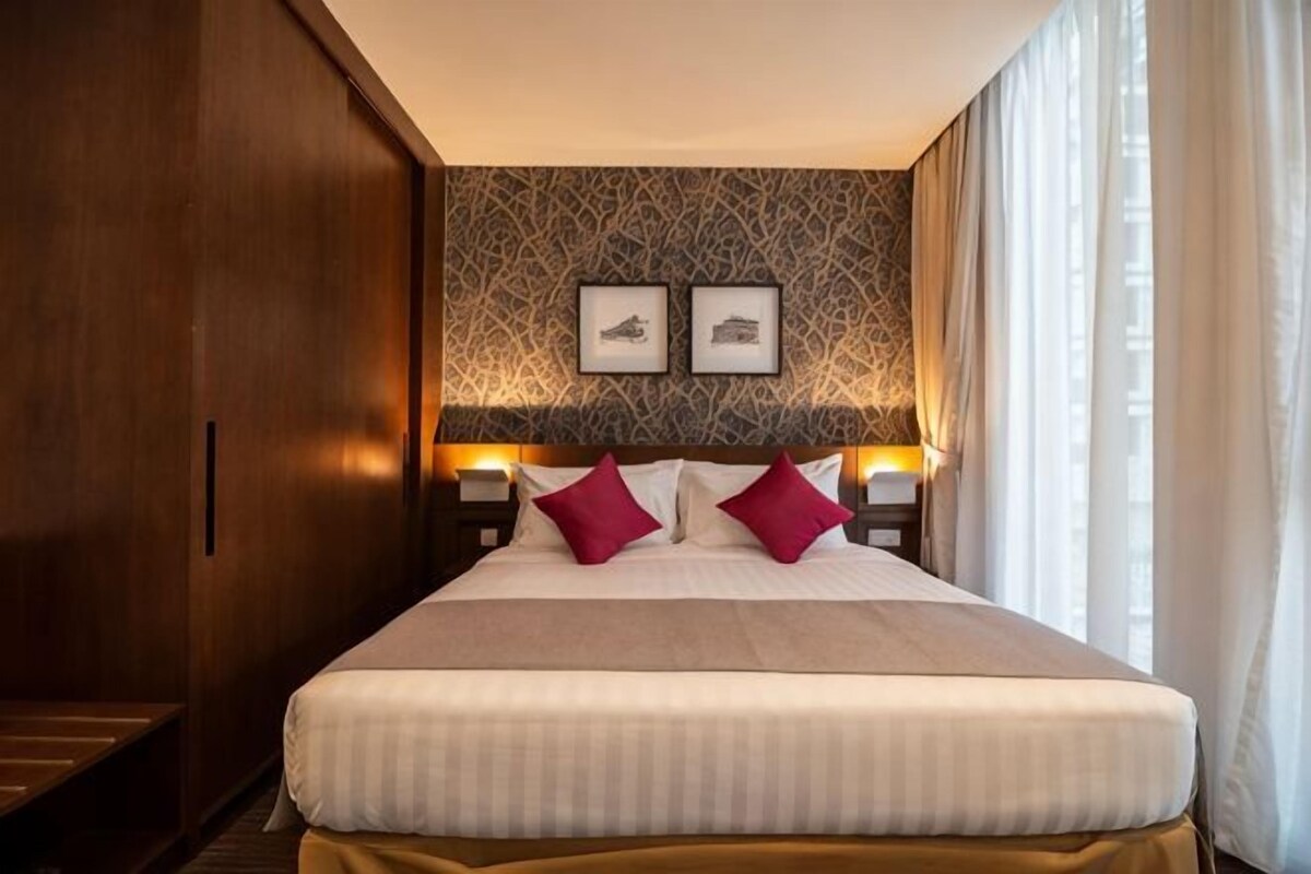 Une chambre d’hôtel avec un grand lit, deux tables de chevet avec des lampes, un mur décoré d’un motif et deux tableaux encadrés au-dessus du lit.