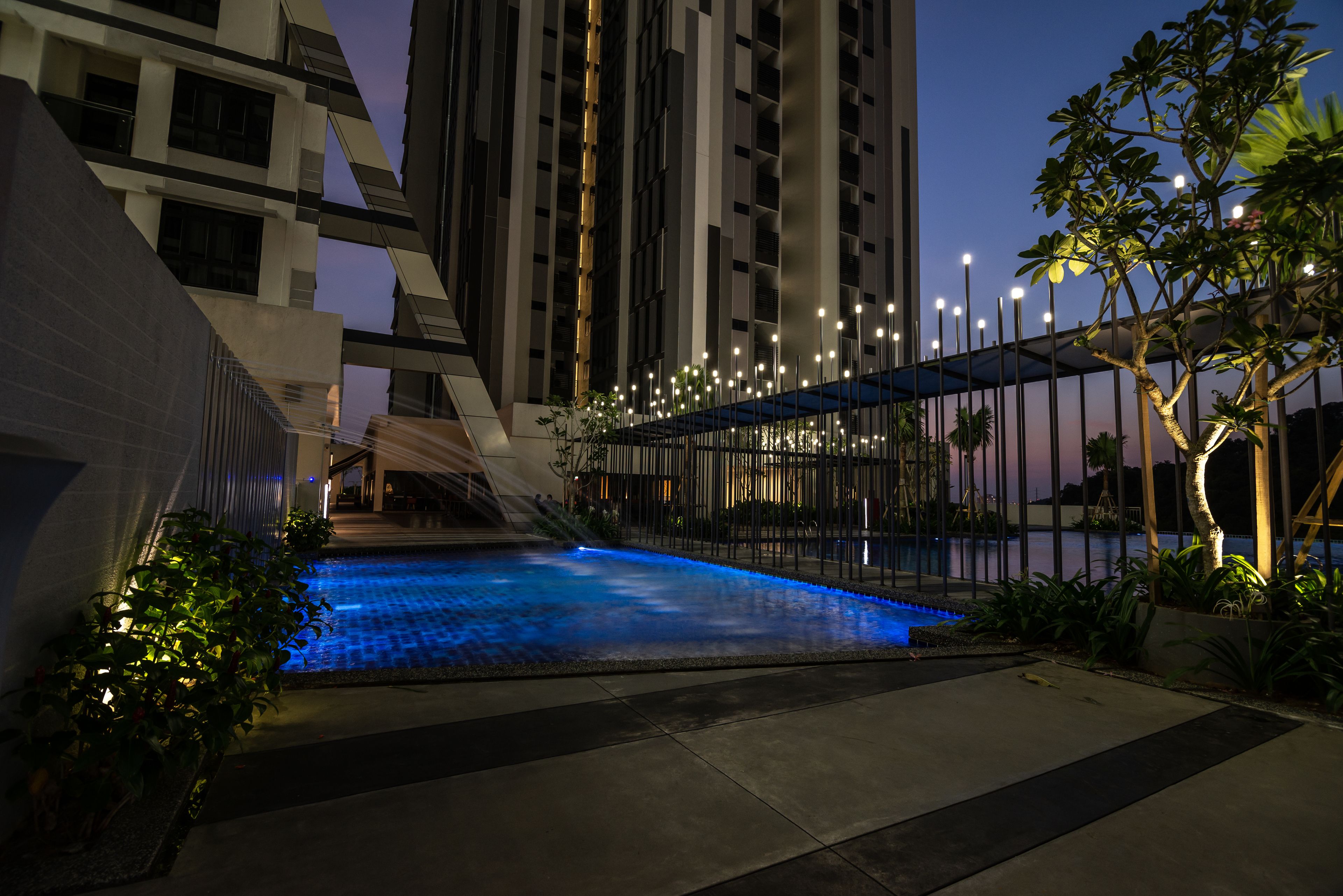 A modern outdoor pool area with a geometric pool design, surrounded by tall buildings and streetlights.