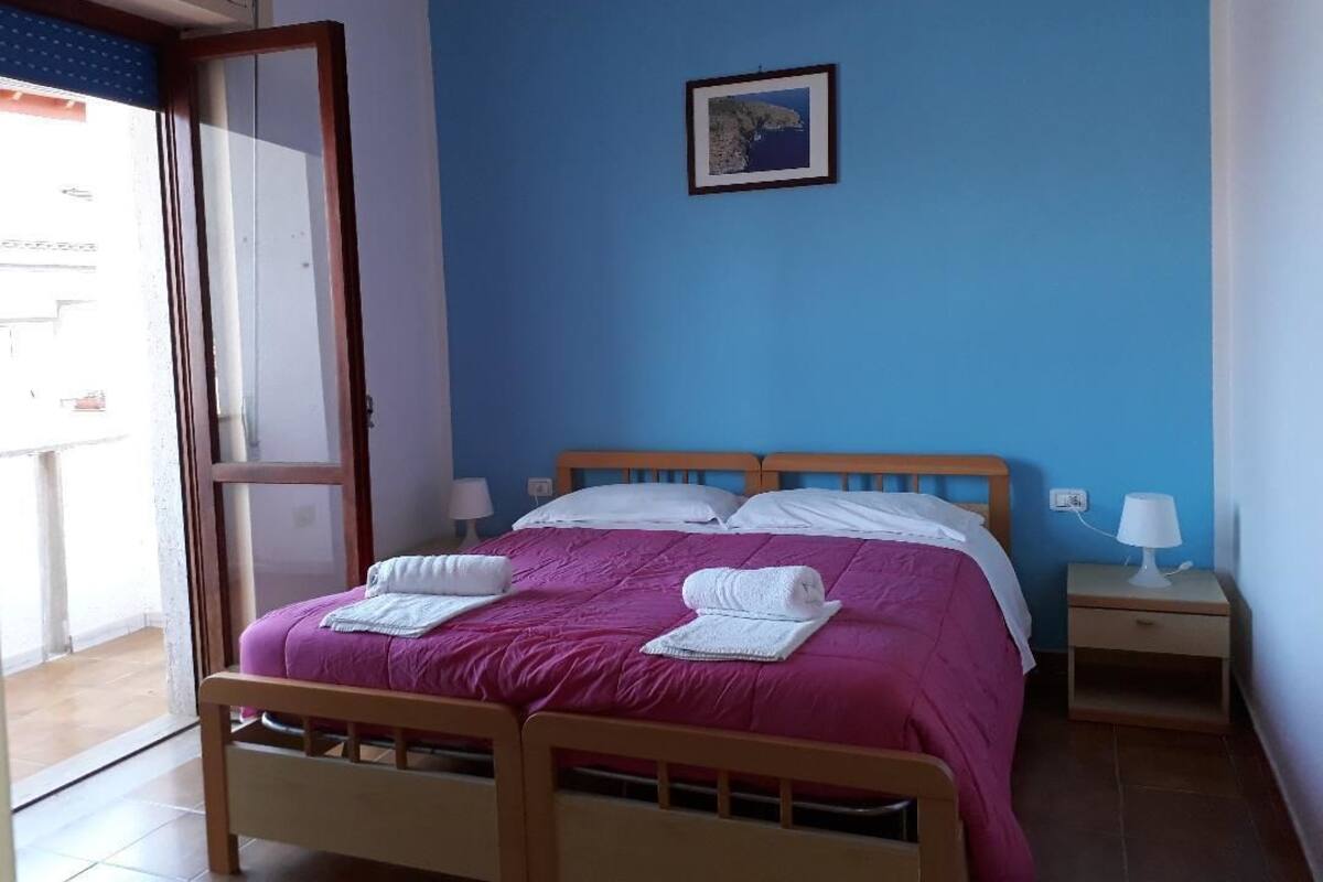 A room with a bed, a nightstand, a wall-mounted picture, and a door leading to an outdoor area.