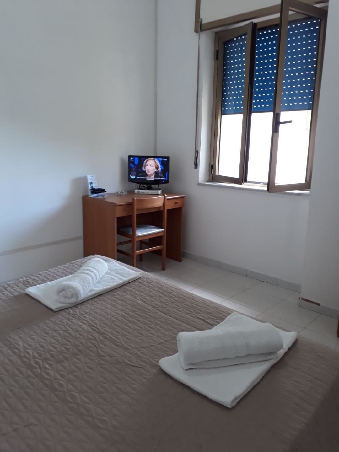 Una habitación de hotel con cama, escritorio, televisor y ventana con persianas.