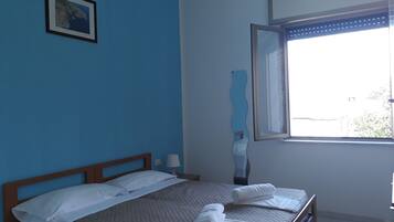 Ein Schlafzimmer mit einem Bett, einem Fenster, einem Bild an der Wand und einem Nachttisch mit einer Lampe.