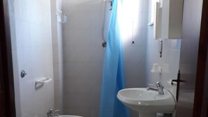 A small, clean bathroom with two toilets, a sink, and a shower. - Pensione Nettuno (Centola)