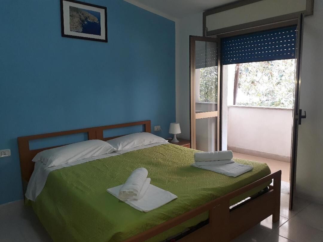 Una camera da letto con una coperta verde, cuscini bianchi e asciugamani ordinatamente piegati.