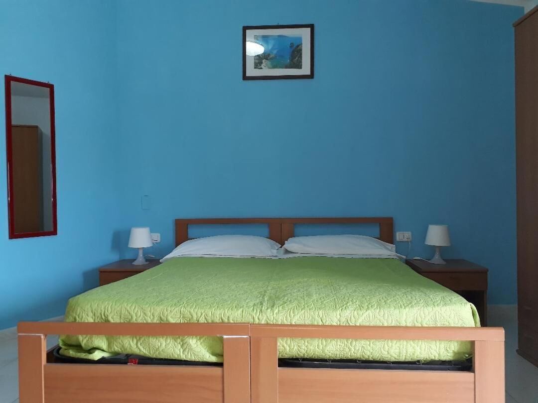 Una habitación con una cama, dos mesitas de noche, una lámpara de noche y un cuadro en la pared, además de un espejo.