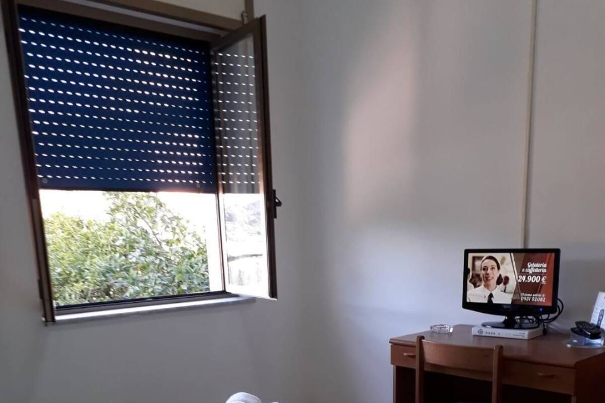 A hotel room with a bed, a desk, a computer, and a window with blinds.