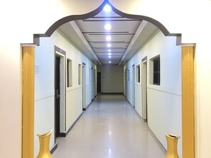 Un long couloir étroit, avec des portes de part et d’autre, un plafond doté d’un éclairage encastré et un plancher poli.