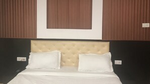 A hotel room with a tufted headboard, two white pillows, and a bed with white bedding. - Hotel Mangalam Palace - Lucknow Airport (Lucknow)