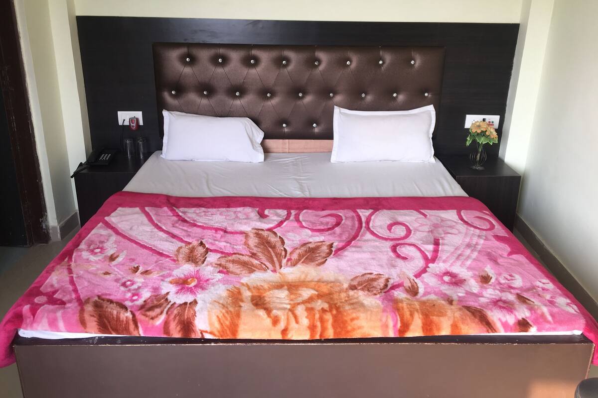 A neatly made bed with a floral bedspread, a tufted headboard, and two bedside tables with lamps and a vase of flowers.