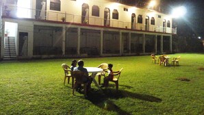 An outdoor dining area with tables and chairs, a building with multiple windows and a balcony, and a well-lit environment. - Hotel Mangalam Palace - Lucknow Airport (Lucknow)