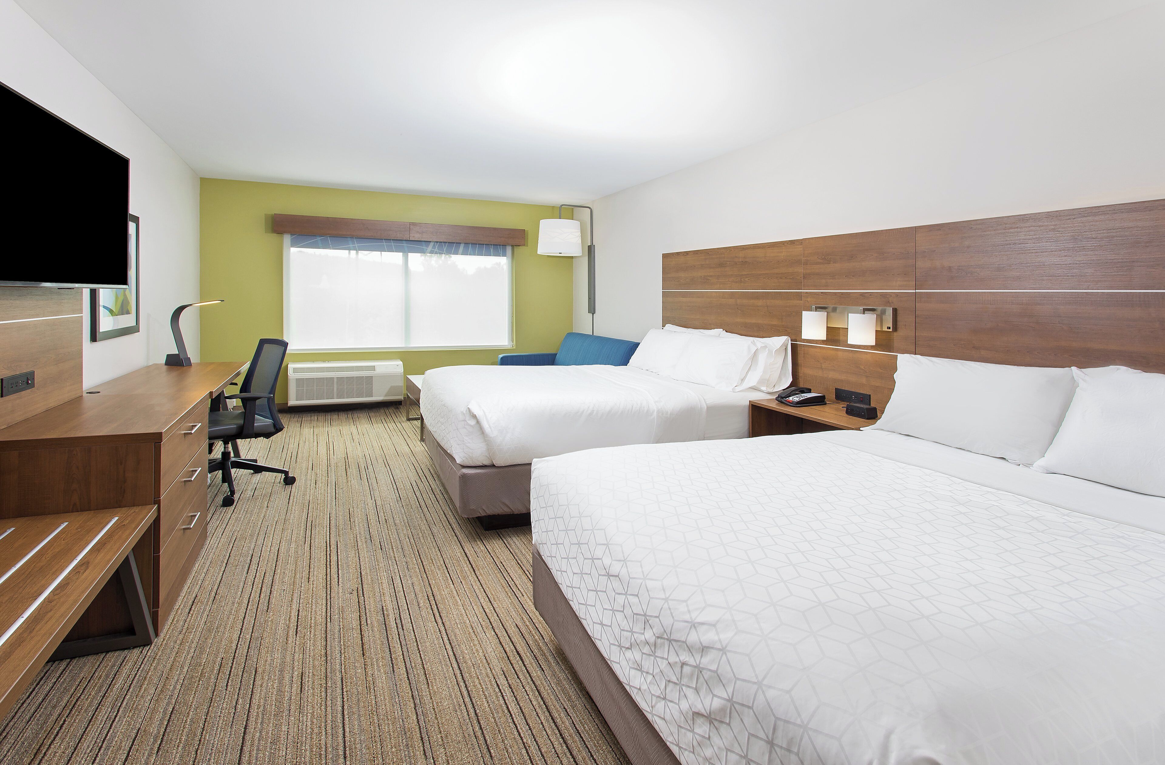 A hotel room with two beds, a desk, a chair, a TV, and a window with blinds.