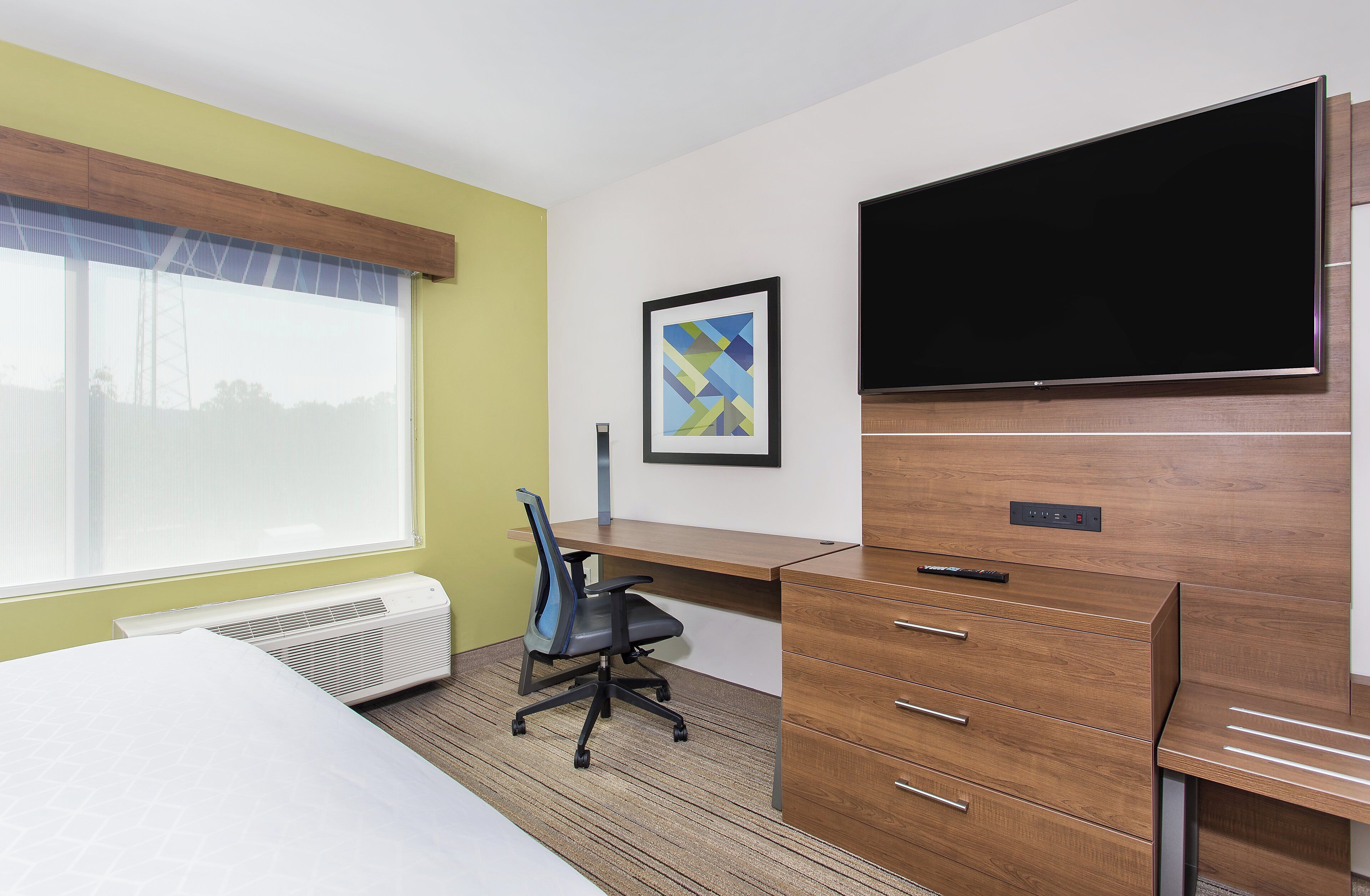 Une chambre d’hôtel équipée d’un lit, d’un bureau, d’une chaise, d’une télévision et d’une fenêtre avec des stores.