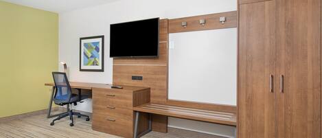A room with a wooden desk, a chair, a television, a wardrobe, and a framed picture on the wall.