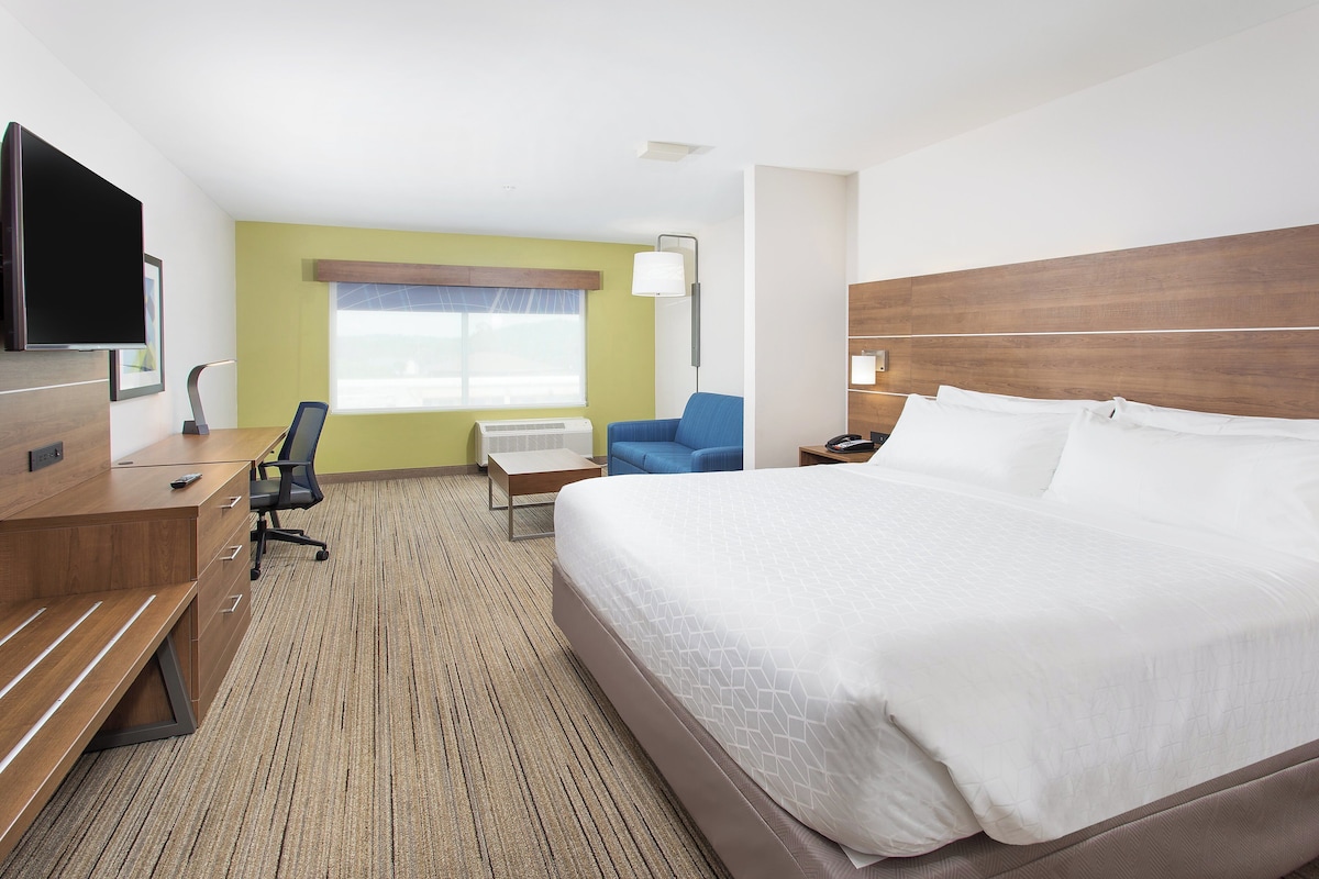 A hotel room with a large bed, a desk with a chair, a television, and a window with blinds.