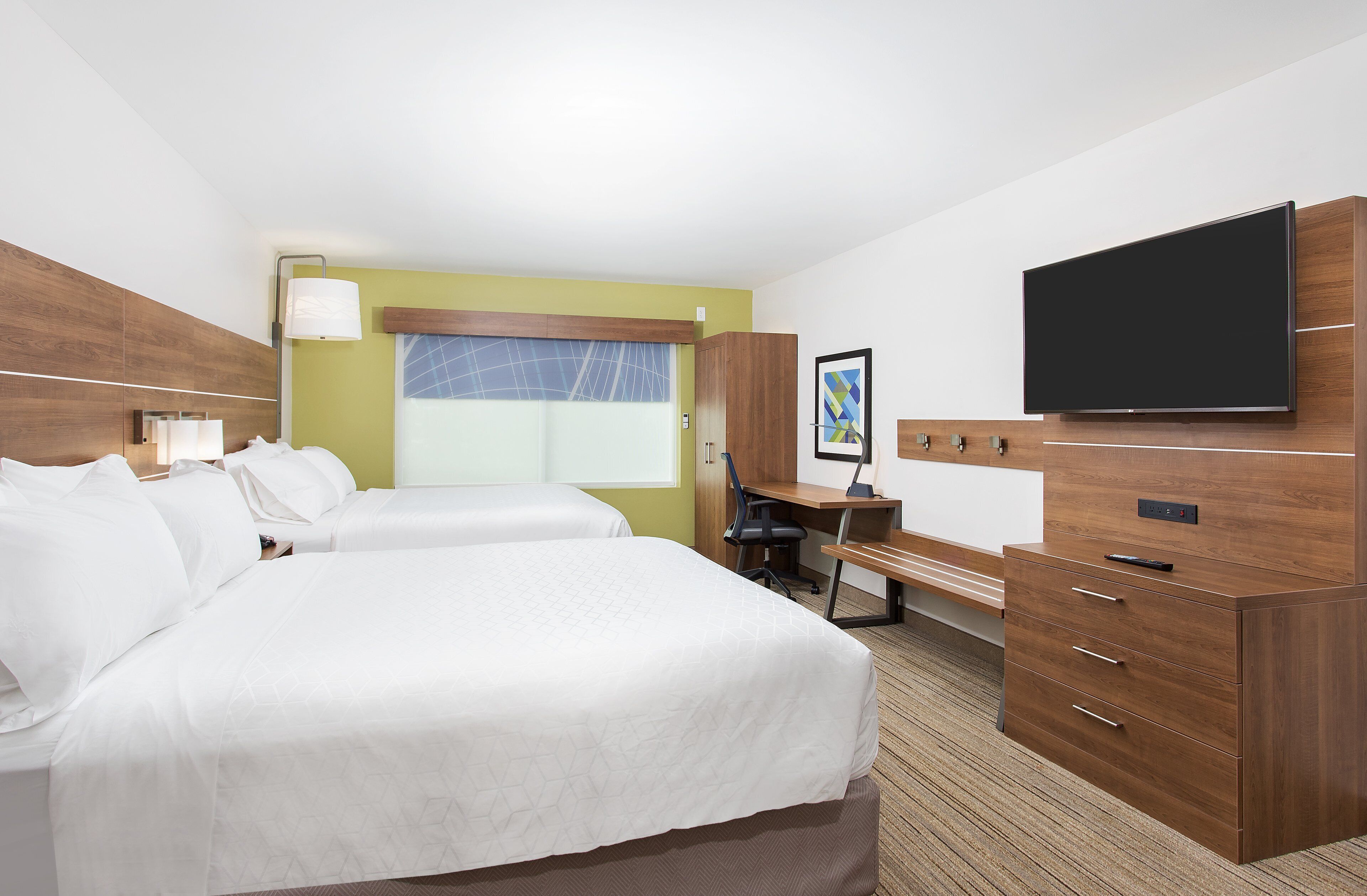 A hotel room with two beds, a desk, a chair, a TV, and a wardrobe.