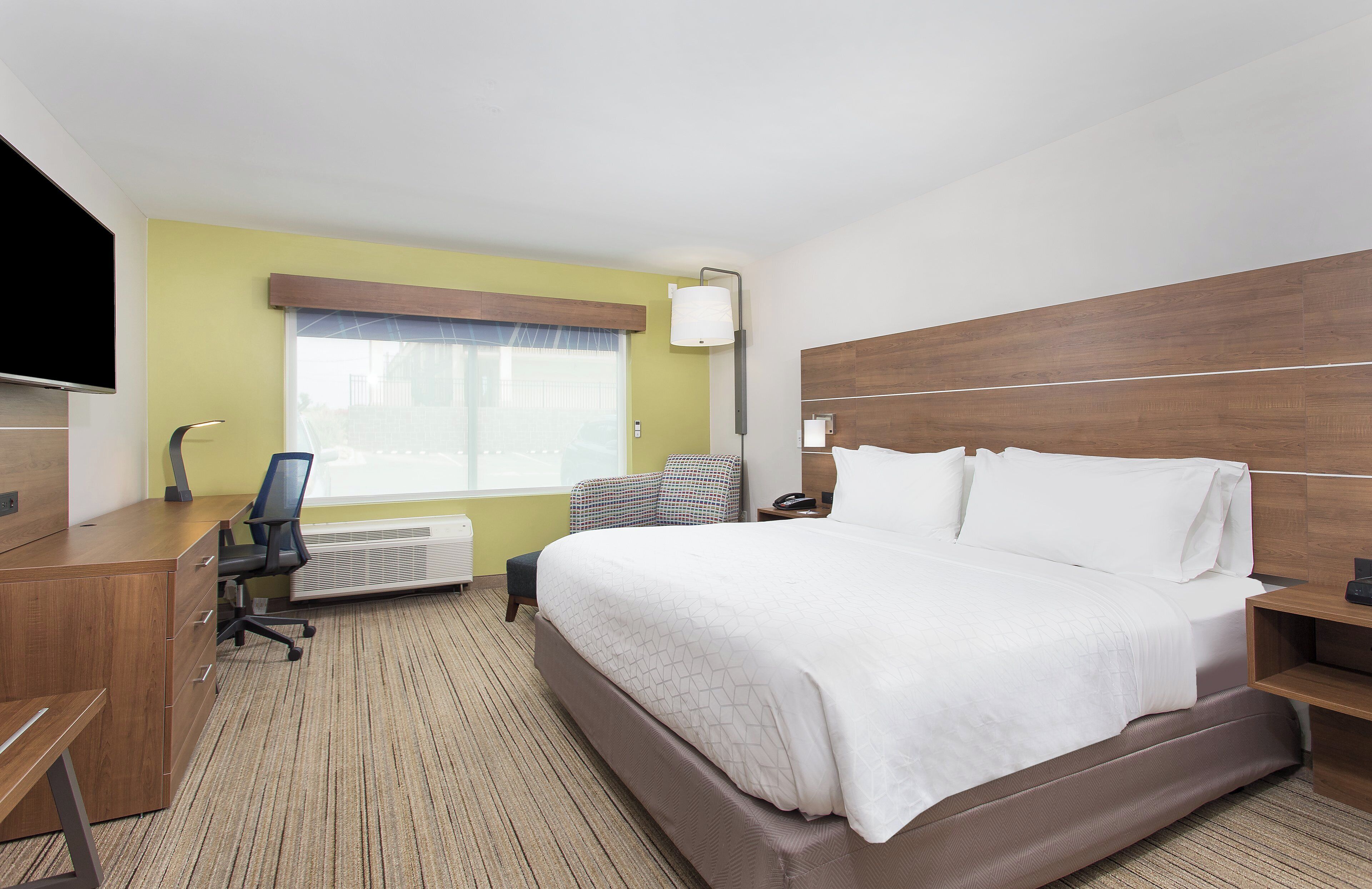 A hotel room with a bed, desk, chair, TV, and a window with blinds.
