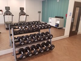 Un gimnasio con cintas de correr, un espejo y una estantería con mancuernas.