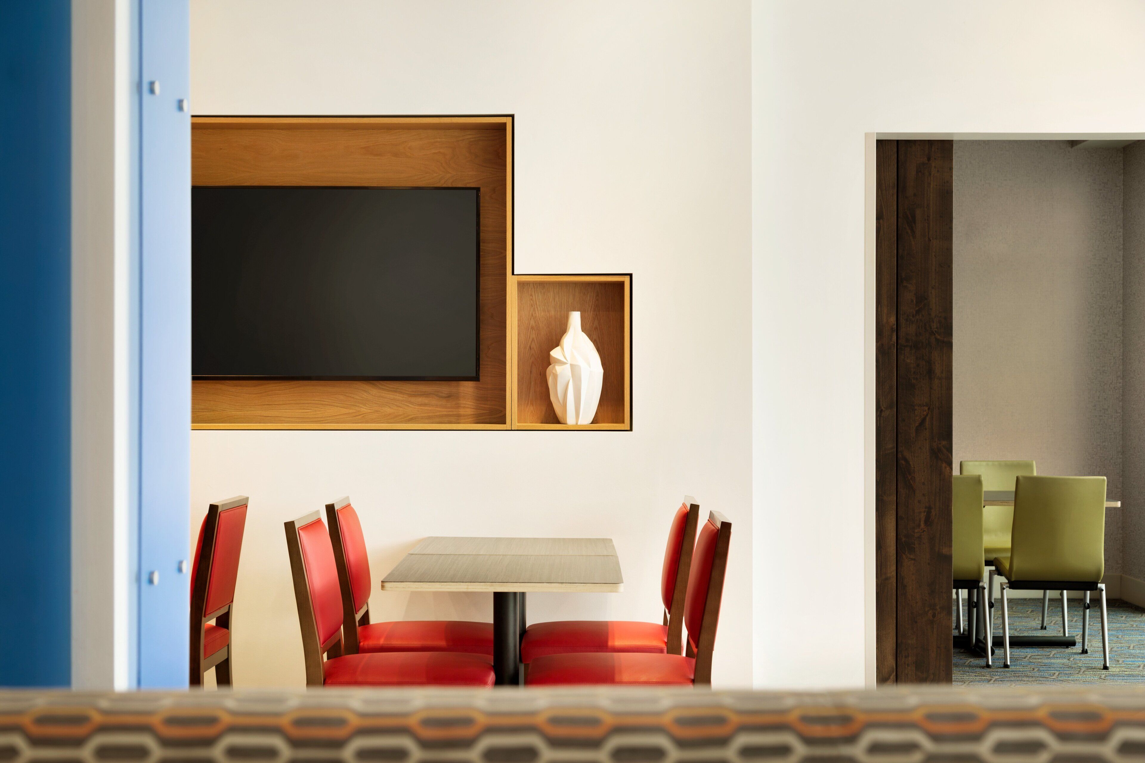 A hotel room with a dining area featuring a table and chairs, a large framed artwork on the wall, and a view into another room with a table and chairs.