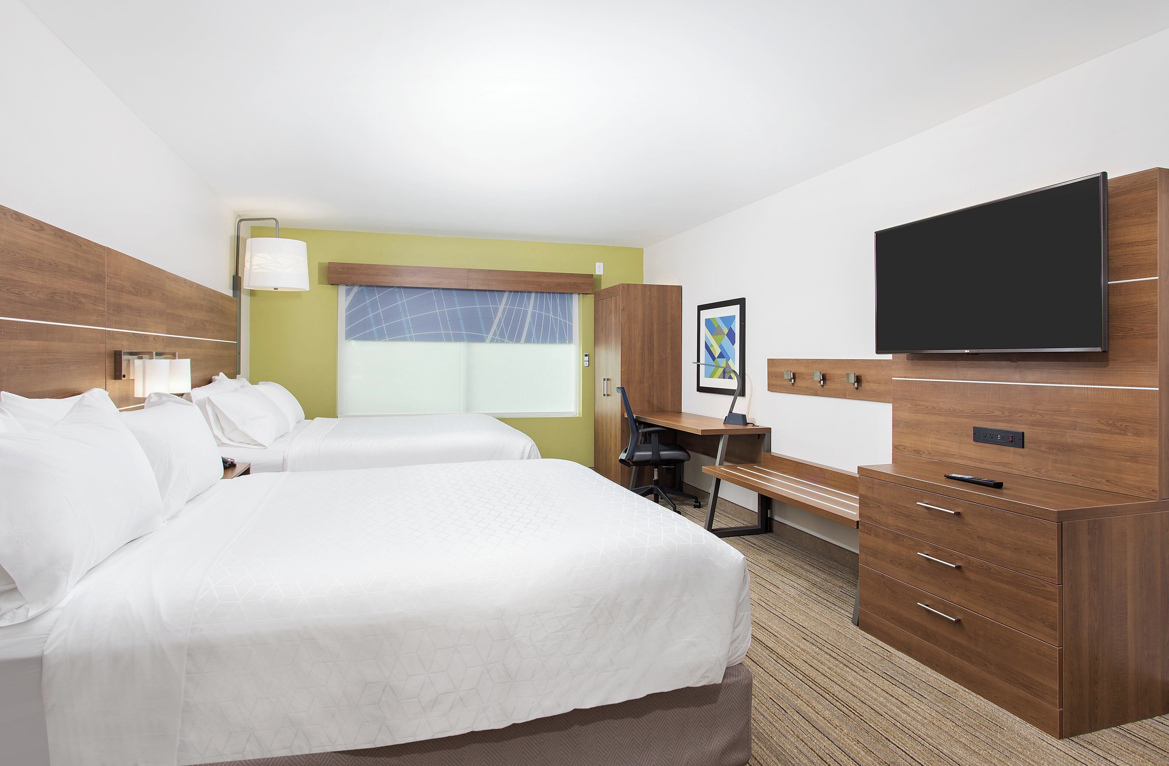 A hotel room with two beds, a desk, a chair, a television, and a window with blinds.