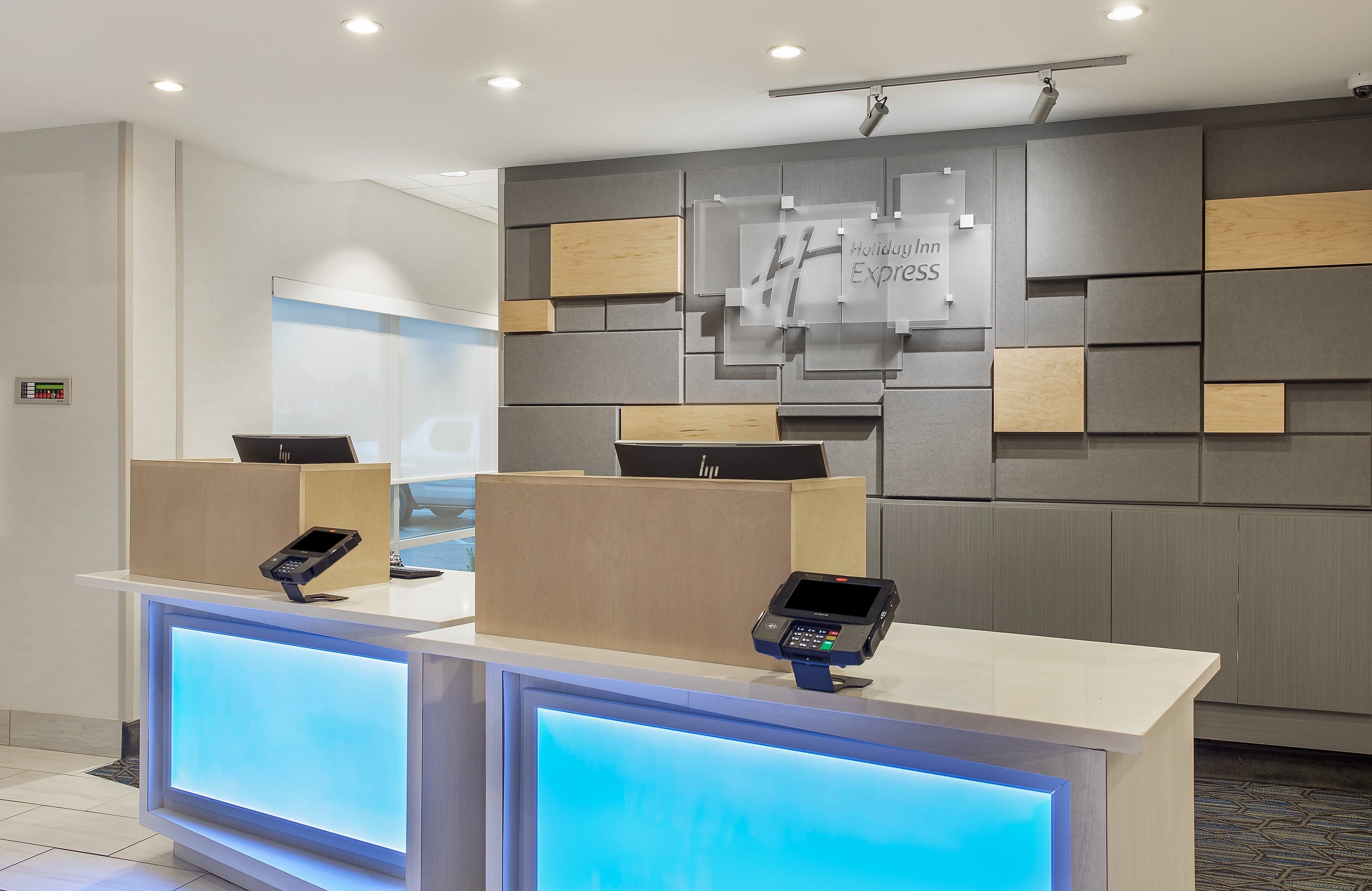 Una recepción de hotel con diseño moderno, que incluye una pantalla digital y un cartel para Holiday Inn Express.