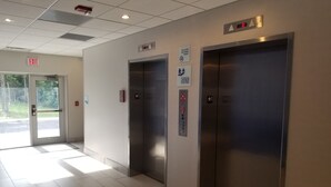 A clean, modern elevator area with two elevators, a clear exit sign, and a digital display showing the floor number.