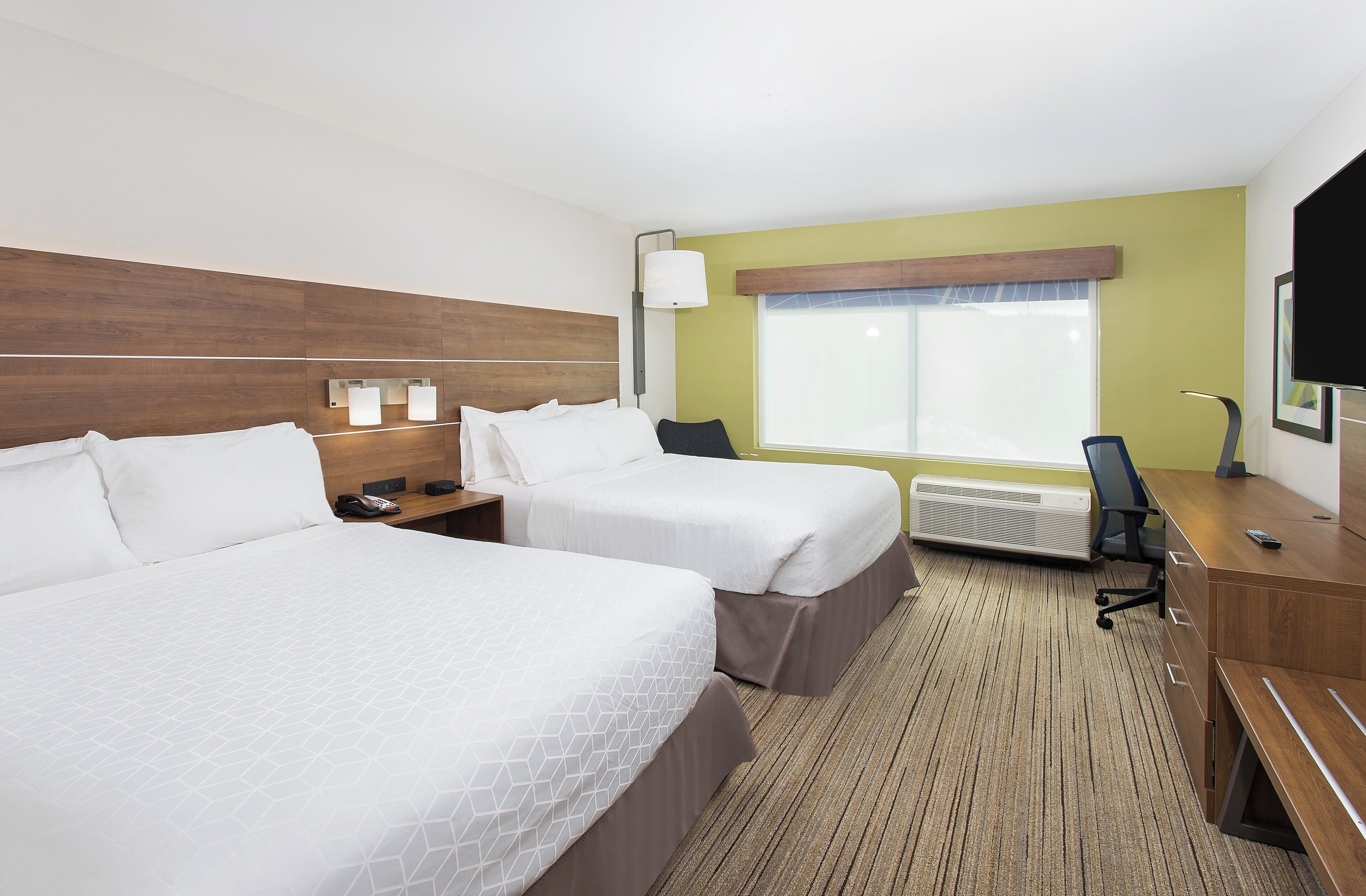 Ein Hotelzimmer mit zwei Betten, einem Schreibtisch, einem Stuhl, einem Fernseher und einem Fenster mit Jalousien.