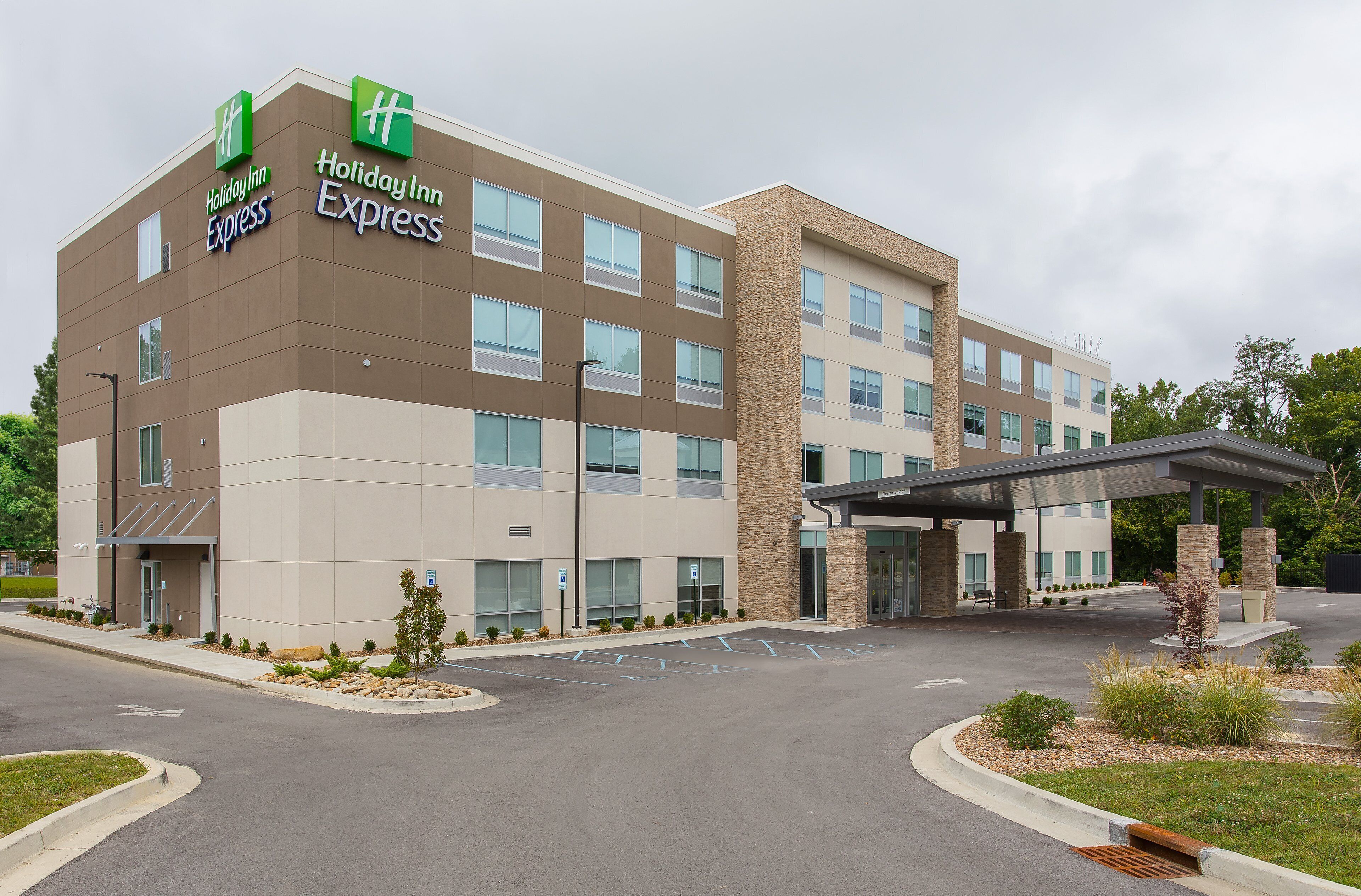 Un hotel Holiday Inn Express con diseño moderno, que presenta un techo plano, grandes ventanales y una entrada cubierta.
