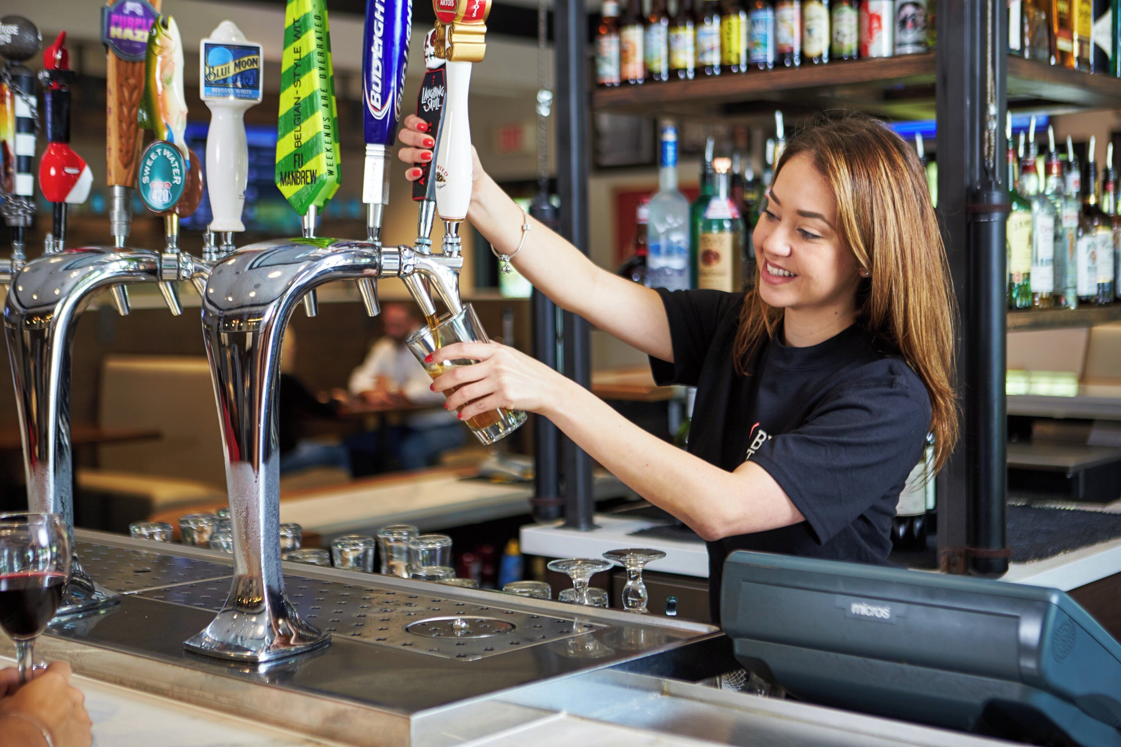 A bartender pouring a drink from a tap labeled 'Blue Moon' into a glass.