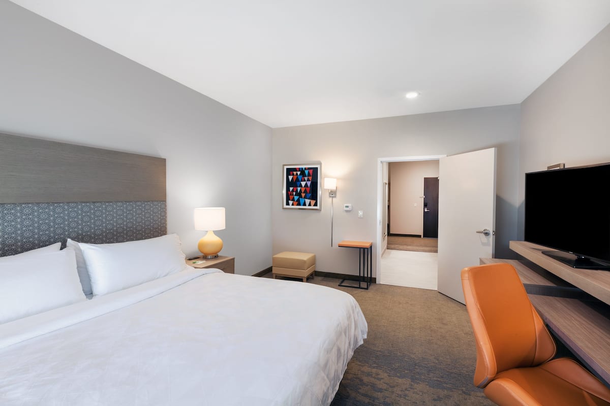 A hotel room with a bed, a desk with a chair, a television, and a small table.