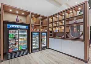 A hotel lobby with two refrigerated beverage displays, a wooden reception desk, and a white storage cabinet.