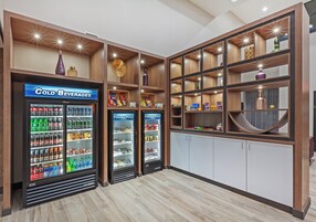 Un hall de hotel con dos mostradores refrigerados para bebidas, un mostrador de recepción de madera y un armario blanco.