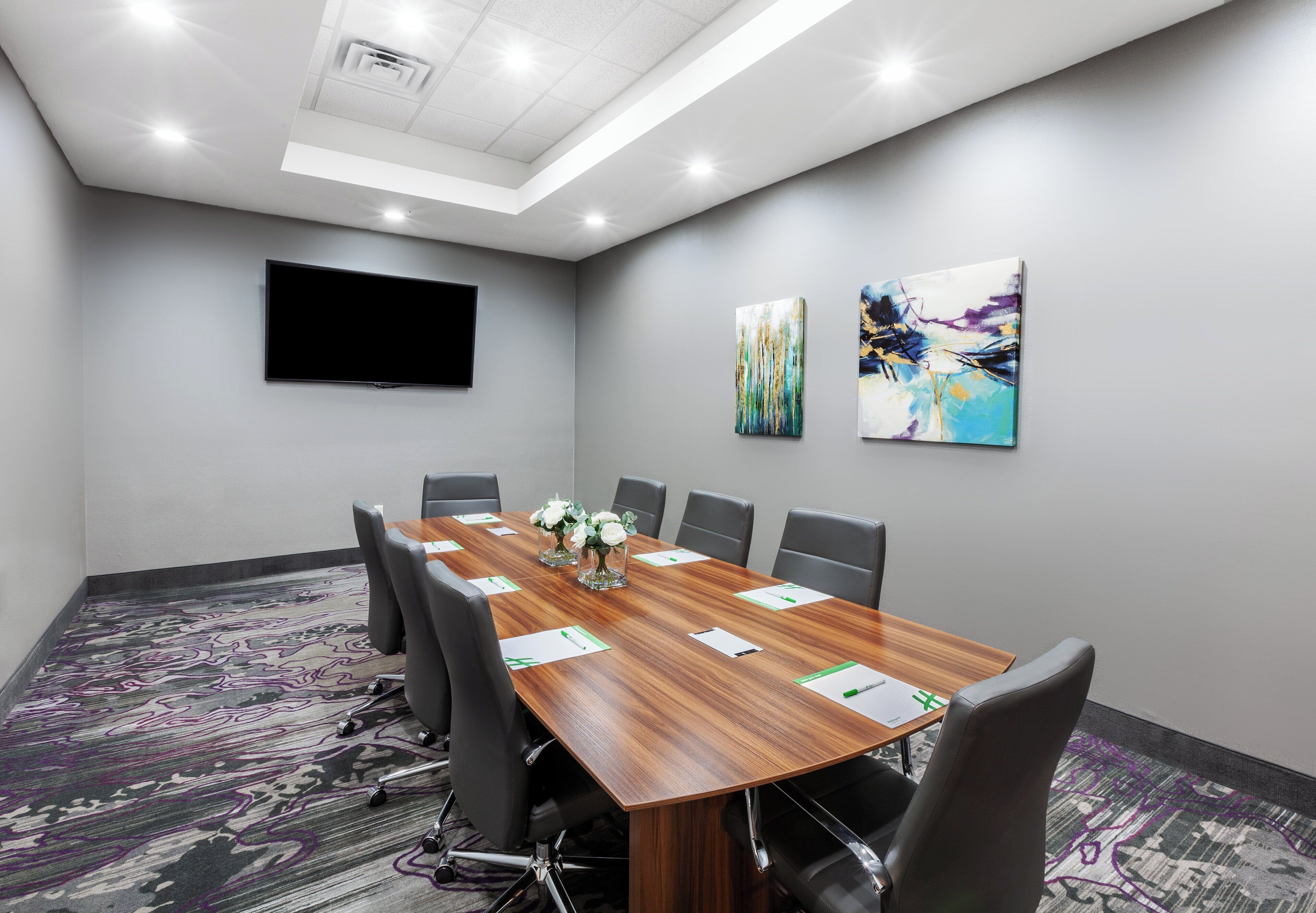 A conference room with a long table, chairs, a flat-screen TV, and abstract art on the walls.